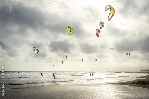 un ciel gris au dessus d'une plage en contre jour avec des voiles  de kitesurf 