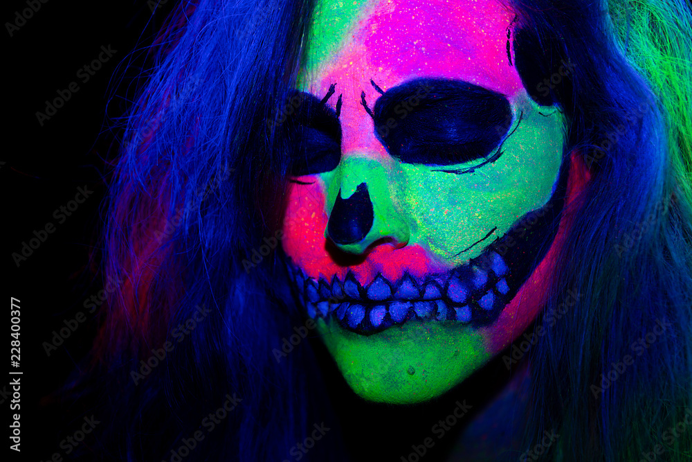 Woman with her face painted with neon make up with a skull design for halloween and santa muerte