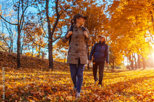 Tourists with backpacks walking in autumn forest. Mother and her adult daughter travelling together