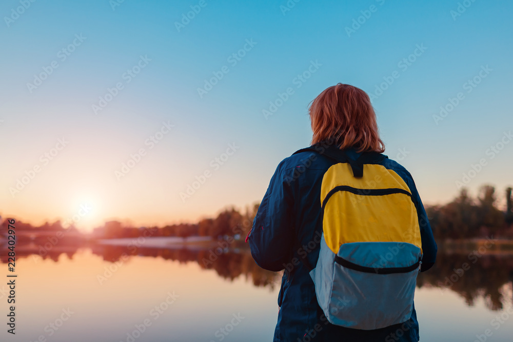 Tourist with backpack walking in autumn forest. Middle-aged woman travelling alone