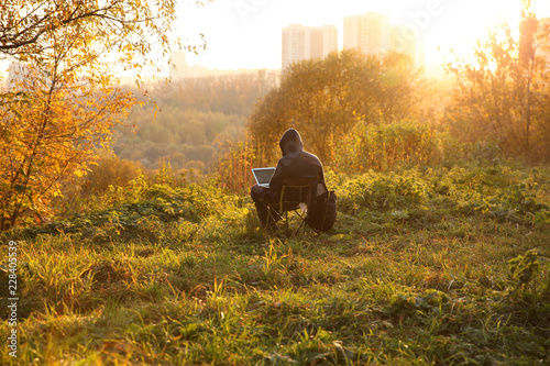 Man works at a laptop in the Park, in the rays of the setting sun.