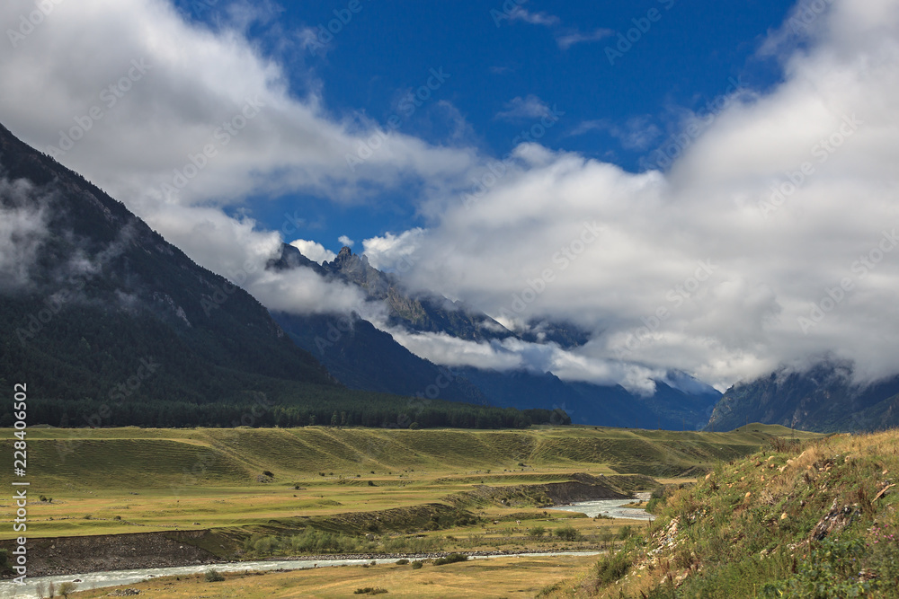 Clouds over the tops of the rocky mountains overgrown with trees. Photographed in the Caucasus, Russia.