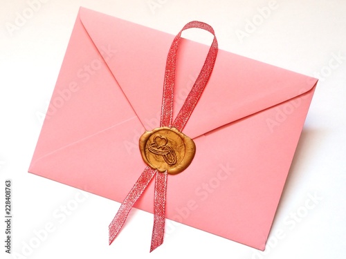 Różowa koperta z lakową złotą pieczęcią z obrączkami oraz czerwoną wstążką