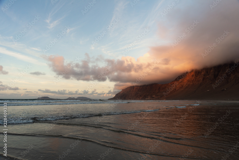 bizarre lines formed by the oncoming waves on a flat shore and a mountain wrapped in clouds at sunset