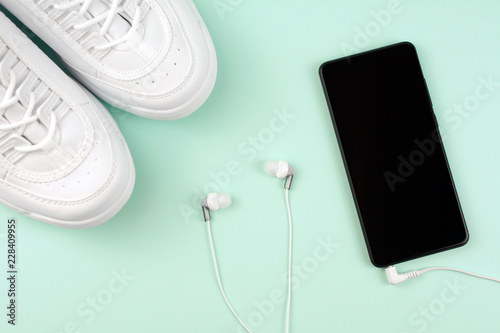 Fitness and sport concept. Sport shoes and mobile phone with headphones. top view blue background