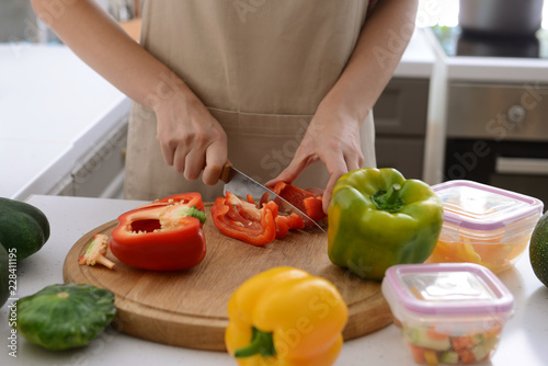 Woman cutting fresh pepper for freezing on wooden board in kitchen