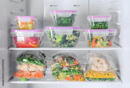 Containers and plastic bags with frozen vegetables in refrigerator