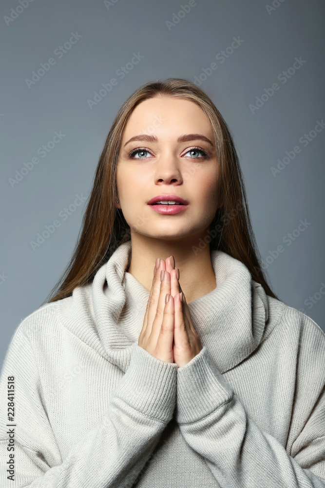 Beautiful young woman praying on grey background Beautiful young woman praying on grey background