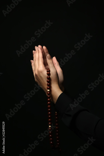 Hands of young religious woman with rosary beads on dark background