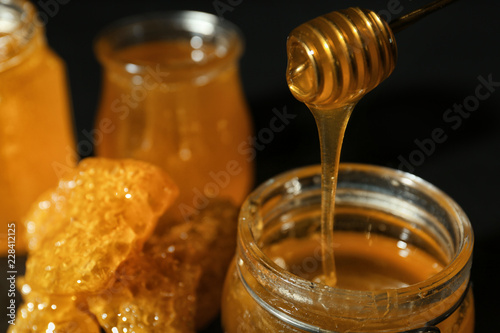 Honey pouring from dipper into glass jar, closeup