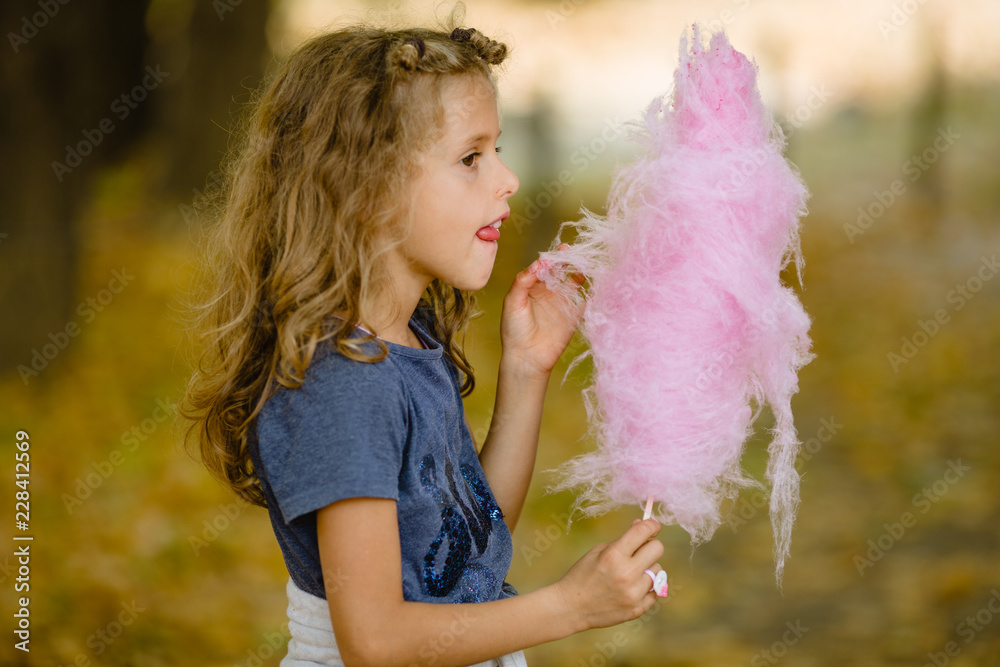 7 year old girl eating cotton candy in park. Shot taken in autumn, fallen  leafs on