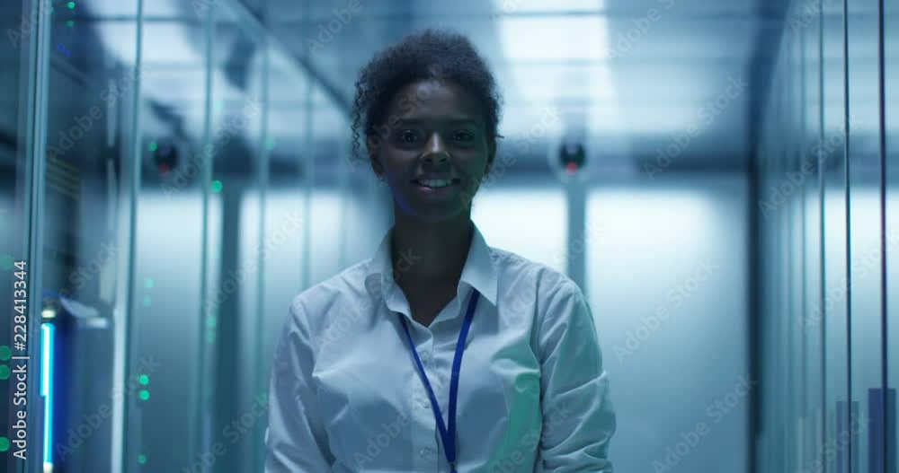 Portrait of African American woman working as IT engineer and standing among server racks in data center room Portrait of African American woman working as IT engineer and standing among server racks in data center room