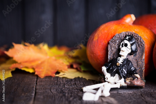 Toy of skeleton with grave, pumpkin and maple leaves on wooden background