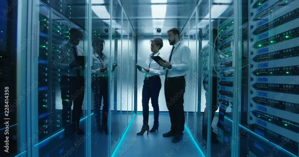 Side view of multiethnic man and woman with tablets coworking in data center server room checking hardware