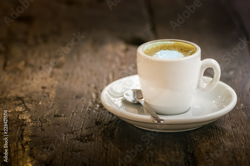 A small espresso coffee cup on a round wooden table outdoors.