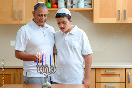 Happy family is lighting a candle for the Jewish holiday Hanukkah. Jewish Dad and teenager son or granfather with granson lighting Chanukkah Candles in a menorah for the holdiays. photo