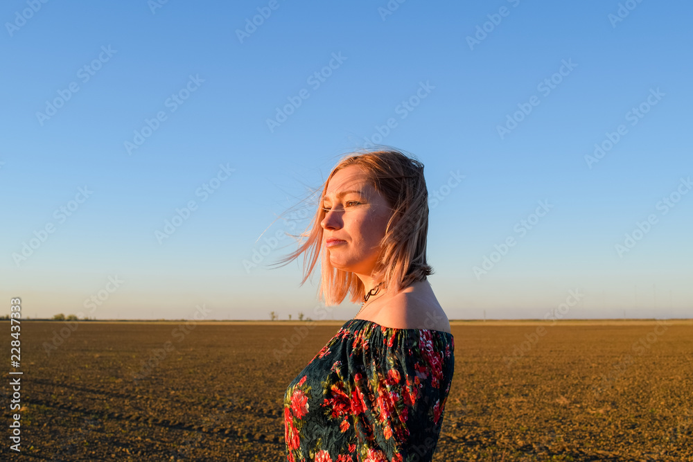 Obraz premium Woman in a plowed field in a red-black dress on a sunset background