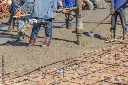 Workers using a wooden spatula for cement after Pouring ready-mixed concrete on steel reinforcement to make the road by mixing mobile the concrete mixer.