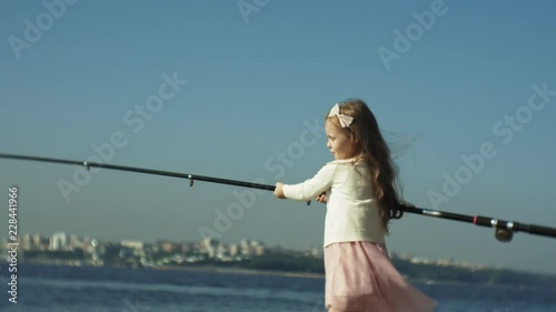 Cute little girl is playing with a fishing rod on a fishing boat near the river