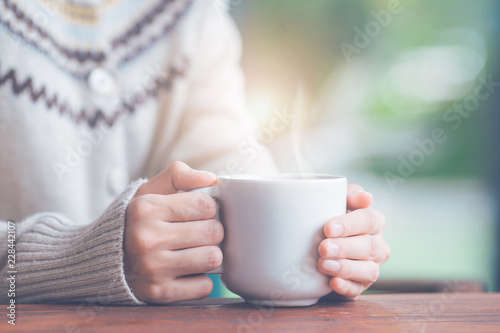 Woman hand in warm sweater holding a cup of coffee.