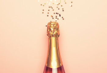 Christmas or New Year pink background with  bottle of sparkling wine, rose champagne and gold decor, top view