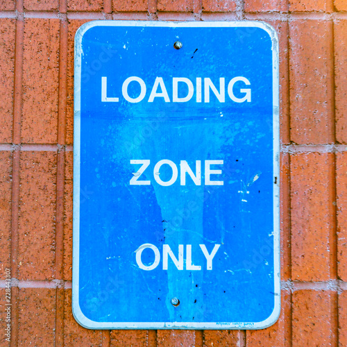 Loading Zone Only Sign nailed to a red brick wall