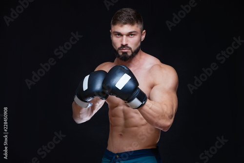 Strong muscular boxer in black boxing gloves. Isolated on black background. © satyrenko