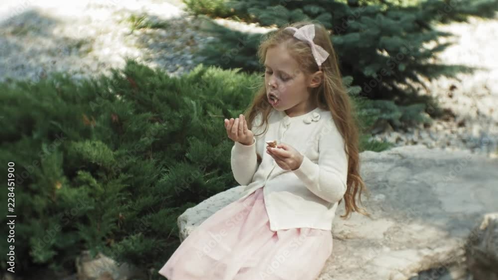 A cute girl is sitting in the park and eating ice cream A cute girl is sitting in the park and eating ice cream