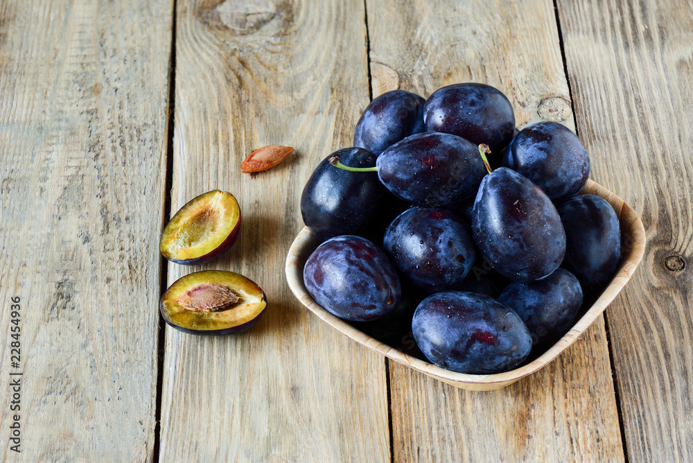 Plum stones. Ripe blue plums with water drops in a wooden bowl on a wooden background Plum stones. Ripe blue plums with water drops in a wooden bowl on a wooden background
