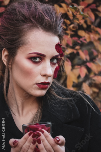 Beautiful young girl with applique red roses flowers on the face in nature autumn