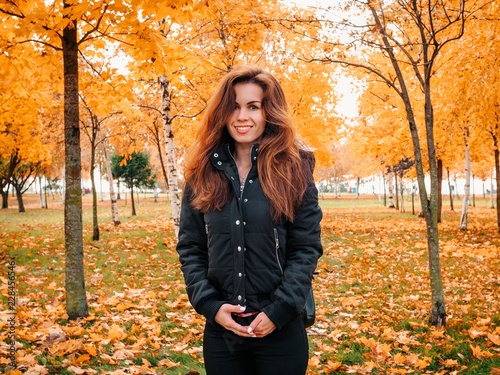 Brunette girl with long hair and jacket standing in autumn yellow forest or Park