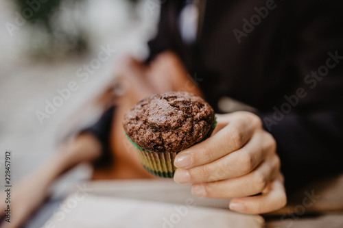 Girl's hand holding a chocolate muffin or cupcake. Blurry backround
