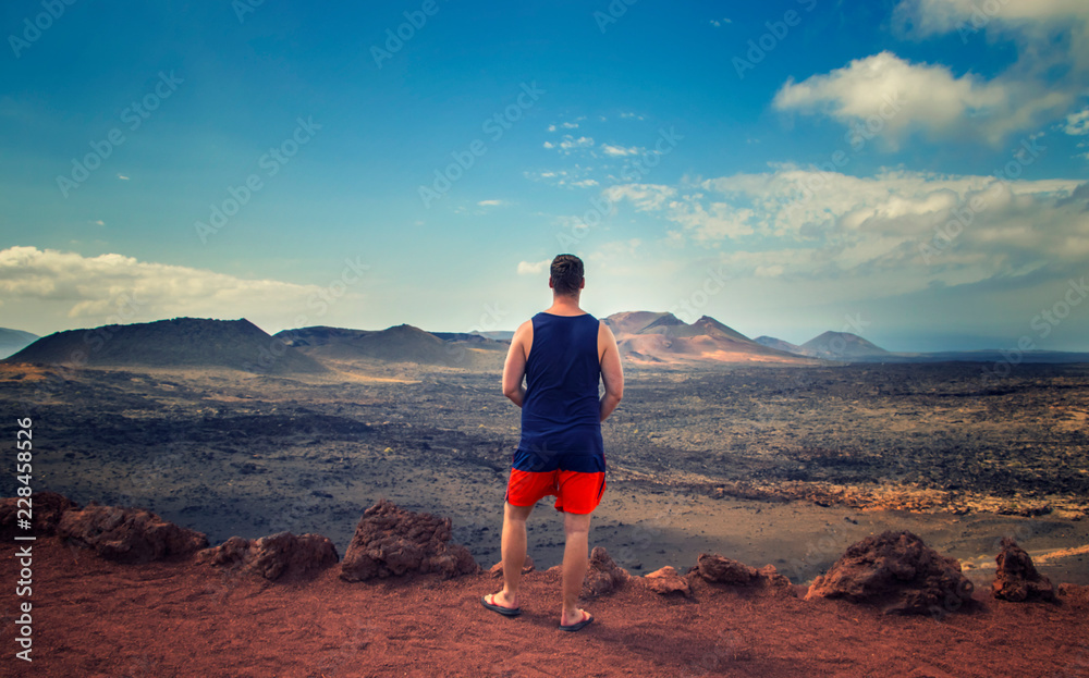 The tourist is standing on the edge of the rock and looks at the red mountains in the national park Timanfaya in Lanzarote, Canary islands. 