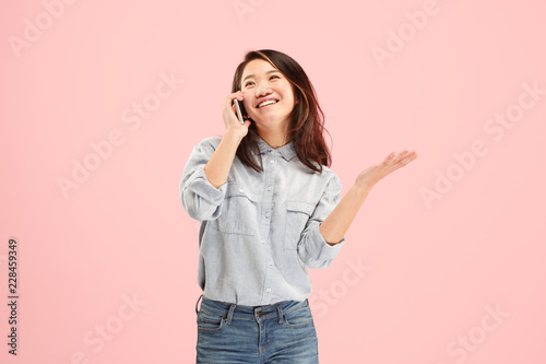 Young beautiful woman using mobile phone studio on pink color studio background. Human facial emotions concept. Trendy colors