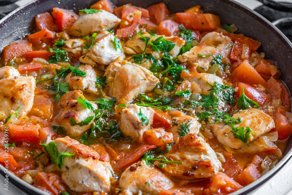 Chicken cacciatore is cooked in a frying pan, chicken stew with tomatoes and red pepper - top view Chicken cacciatore is cooked in a frying pan, chicken stew with tomatoes and red pepper - top view