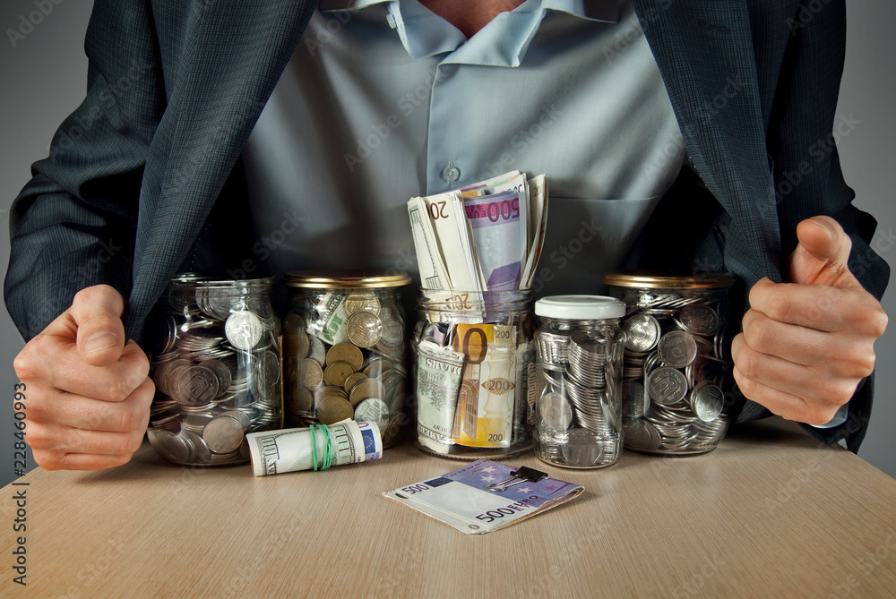 A man in a suit conserved money in glass jars. The concept is the storage of money, stocks at difficult times. Conserve money instead of vegetables. A man in a suit conserved money in glass jars. The concept is the storage of money, stocks at difficult times. Conserve money instead of vegetables.