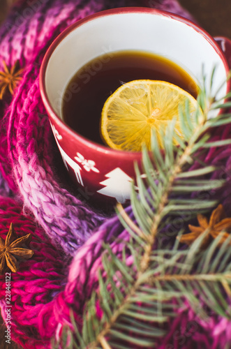 Cup of lemon tea covered with scarf. Christmas tree in background. Winter concept.