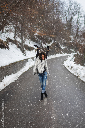 Young black woman dancing and having fun under the snow in cold winter.