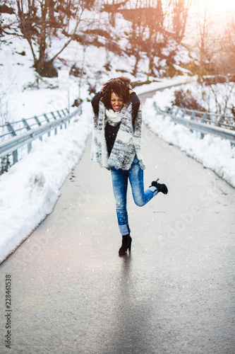 Young black woman dancing and having fun under the snow in cold winter.