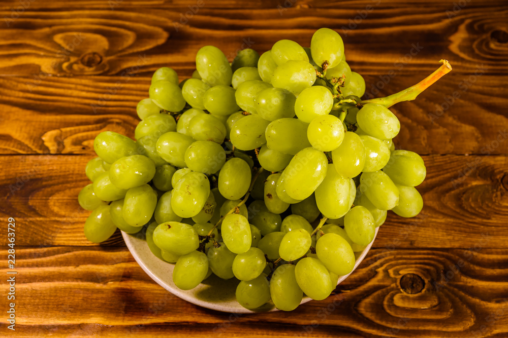 Ceramic plate with green grapes on wooden table Ceramic plate with green grapes on wooden table