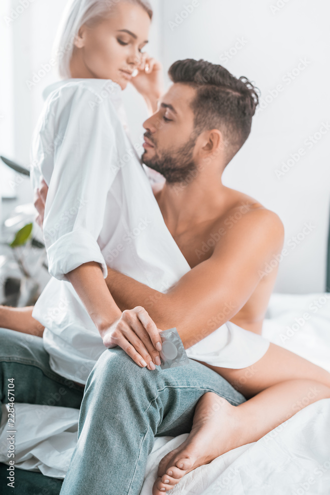 passionate young couple with condom sitting on bed passionate young couple with condom sitting on bed