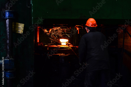 Hot iron in smeltery held by a worker. Iron melting recycling work. Metallurgical production, manufacturing premises, workshop at the plant, blast furnace, heavy industry, engineering, steelmaking.