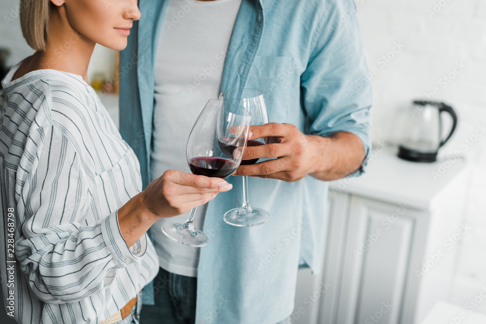 cropped image of young couple clinking with wineglasses in kitchen cropped image of young couple clinking with wineglasses in kitchen