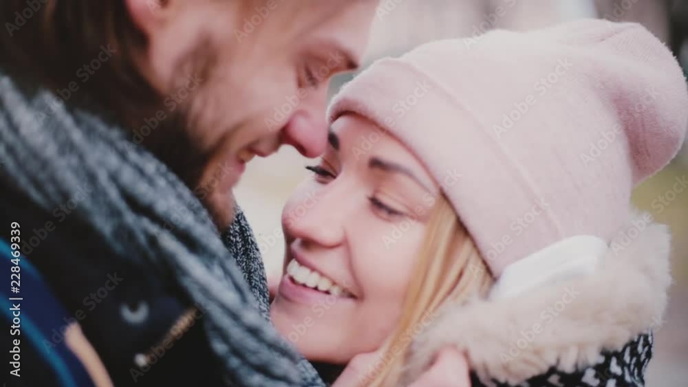 Close-up view of happy smiling young European romantic couple stand close together and talking outside on a cold day. Close-up view of happy smiling young European romantic couple stand close together and talking outside on a cold day.