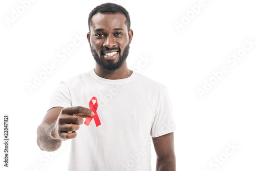 smiling african american man in blank white t-shirt holding aids awareness red ribbon and looking at camera isolated on white