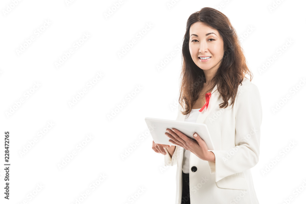 smiling asian businesswoman with aids awareness red ribbon on jacket using tablet and looking at camera isolated on white smiling asian businesswoman with aids awareness red ribbon on jacket using tablet and looking at camera isolated on white