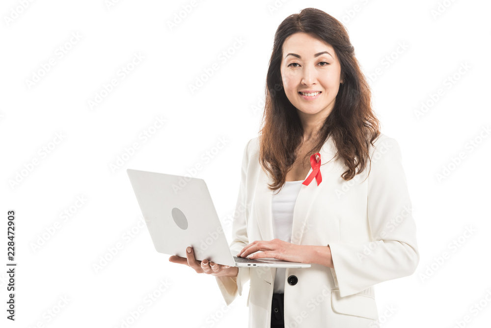happy asian businesswoman with aids awareness red ribbon on jacket using laptop and looking at camera isolated on white happy asian businesswoman with aids awareness red ribbon on jacket using laptop and looking at camera isolated on white