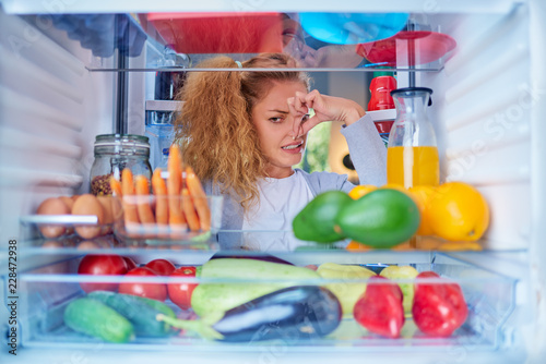 Canvas-taulu Womann standing in front of opened fridge and holding up to her nose because of bad smell