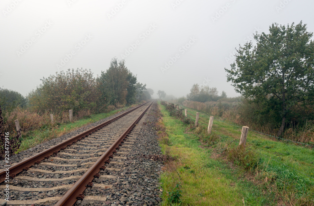 Rusty seemingly endless single track train tracks through a rural Dutch area with early morning fog