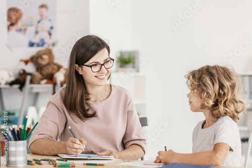 Smiling teacher listening to autistic boy in the classroom